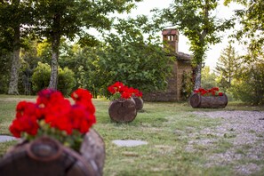 A garden with wooden barrels containing red flowers, a stone building with a tower, and trees in the background.