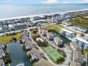 Vista aérea de una zona residencial costera con varias edificaciones de dos pisos, una cancha de tenis y una masa de agua.