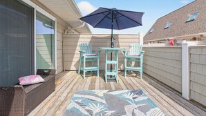 A covered patio with a table and chairs, a large umbrella, and a wicker bench. - Ocean Isle Beach Getaway Is A Slice Of Heaven (Ocean Isle Beach)