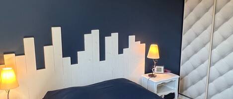 A hotel room with a bed, two bedside tables with lamps, a white headboard, and a quilted wall panel.