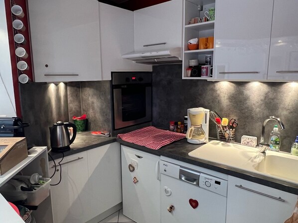 A compact kitchen with white cabinets, a built-in oven, a coffee maker, and a sink.