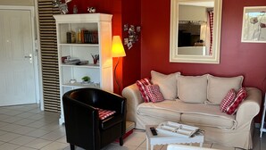 Una sala de estar con un sofá, un sillón negro, una mesita blanca y una estantería.