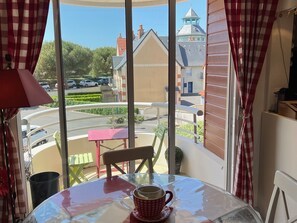 A balcony with a table and chairs, a red and white checkered curtain, and a view of a parking lot and buildings.