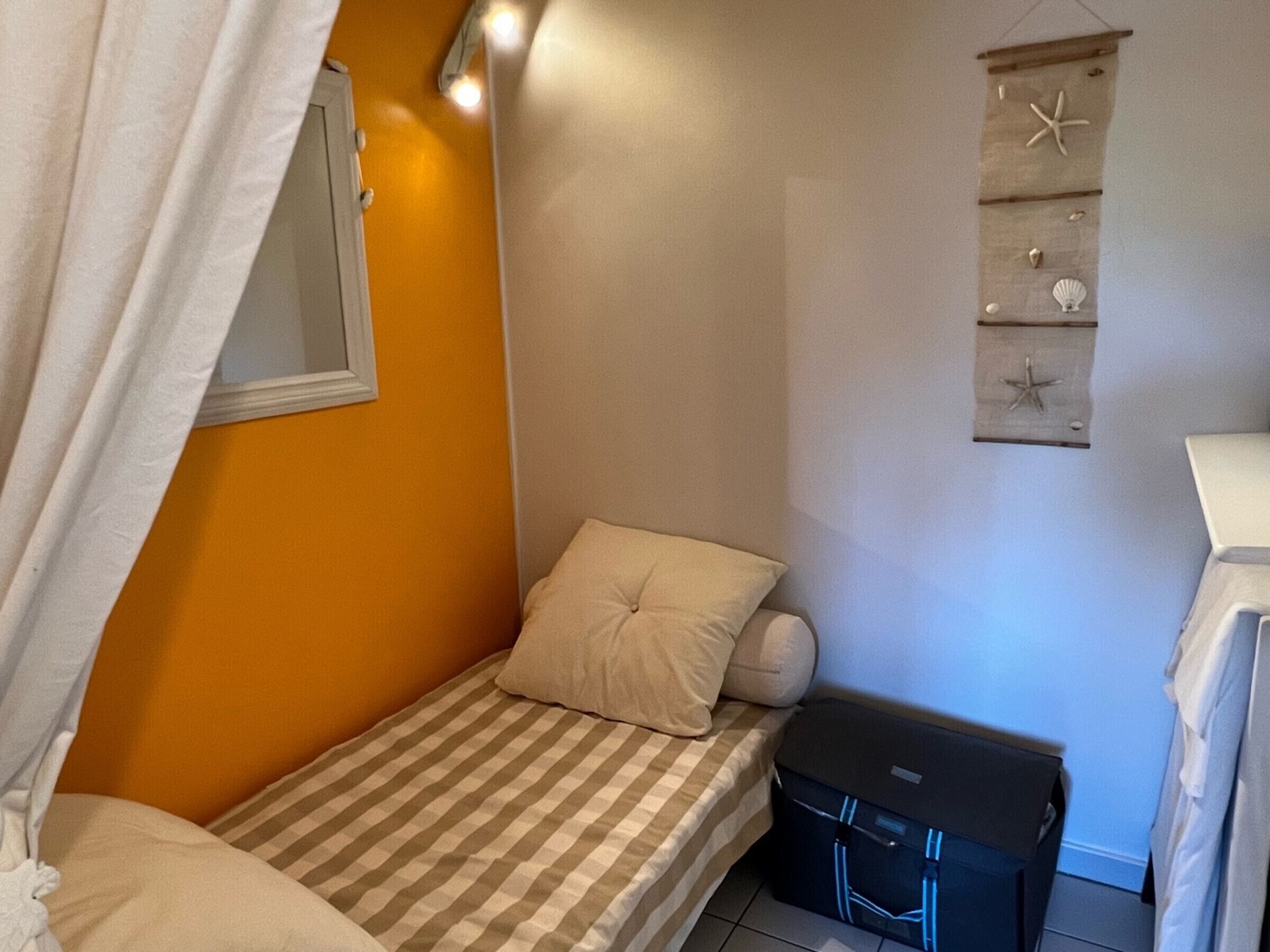 A small, single-bed room with a checkered bedspread, a white pillow, and a suitcase on the floor.