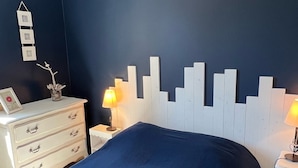 Un dormitorio con cama, cómoda, mesitas de noche y marcos de cuadros en la pared.