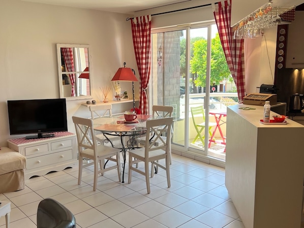 Cozinha moderna com área de jantar, televisão e uma janela grande com cortinas vermelhas.