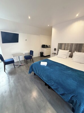 A modern hotel room with a large bed, a desk, two chairs, a TV, and a kitchenette. -  Aux Charmes (Isques)