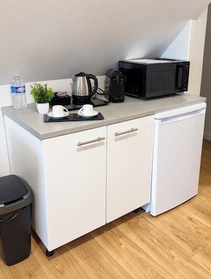 Une petite cuisine équipée comprenant une machine à café, une bouilloire, un four à micro-ondes et une petite plante en pot.