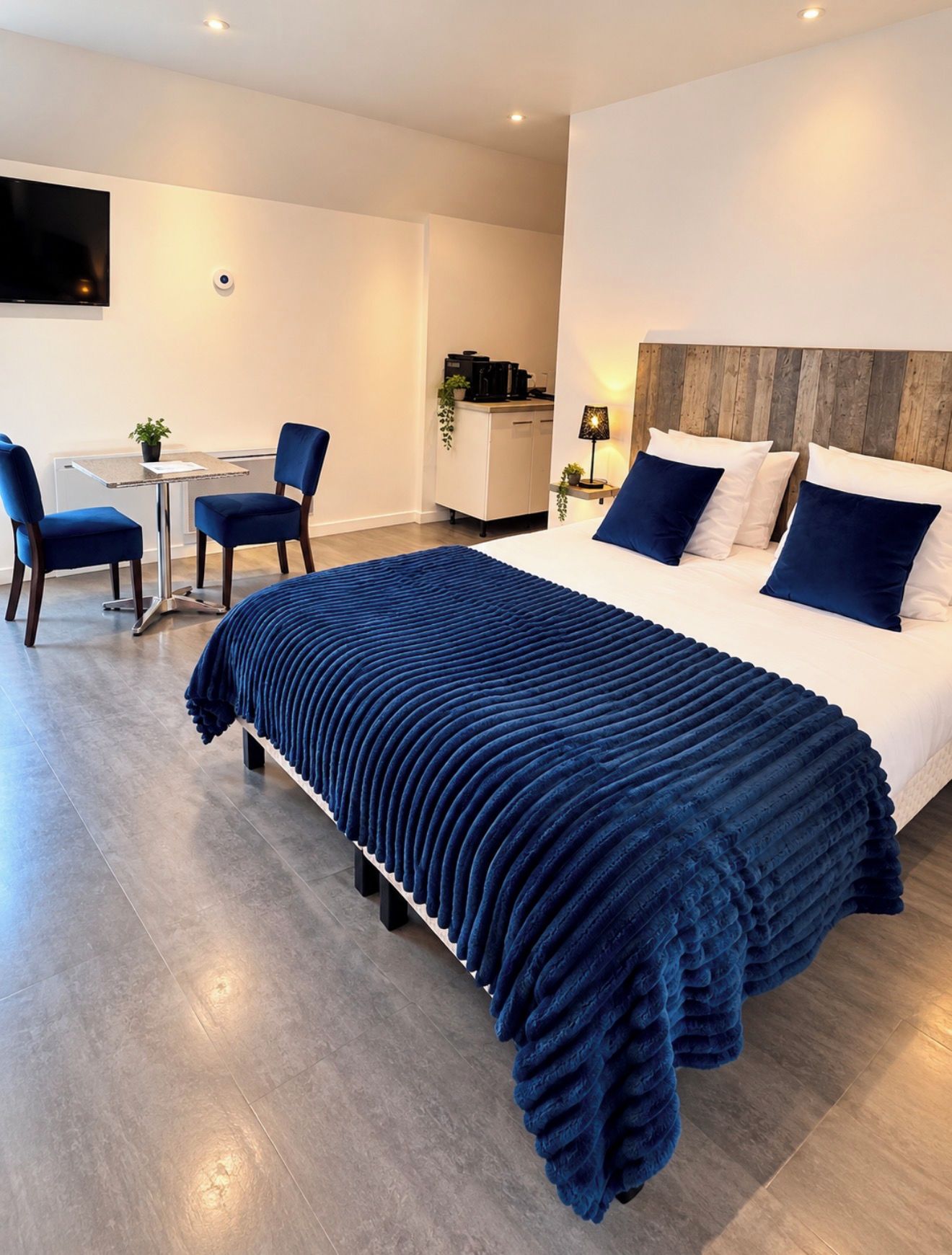 Una habitación de hotel moderna con una cama grande, un escritorio, dos sillas, una mesita y un televisor montado en la pared.