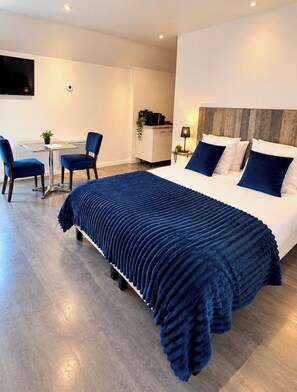 A modern hotel room with a large bed, a desk, two chairs, a small table, and a TV mounted on the wall. -  Aux Charmes (Isques)