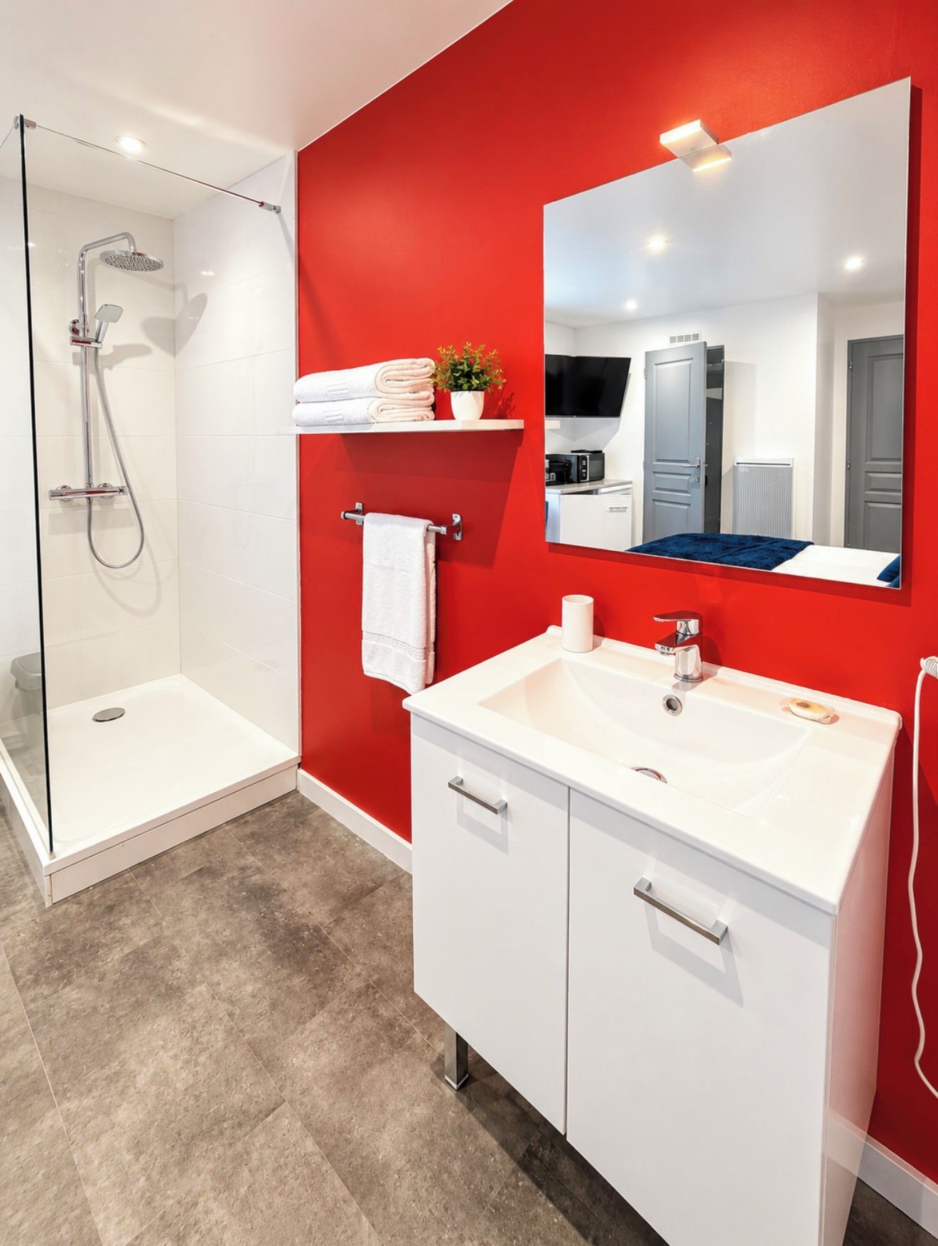 A modern bathroom with a glass shower enclosure, a white sink, and a red accent wall.