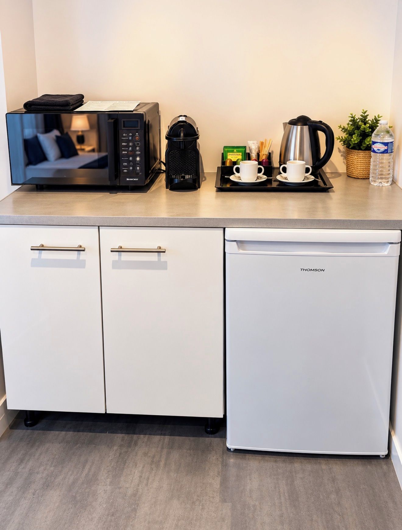 Een kitchenette met een magnetron, koffiezetapparaat en waterkoker op het aanrecht.