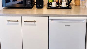 Een kitchenette met een magnetron, koffiezetapparaat en waterkoker op het aanrecht.