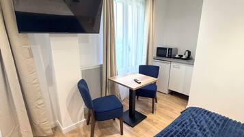 Een hotelkamer met een bed, een aan de muur bevestigde televisie, een klein tafeltje met stoelen, een kitchenette en een raam met gordijnen.