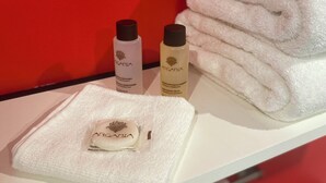 A white towel, two bottles of Argania products, and a folded towel on a white surface against a red background. -  Aux Charmes (Isques)