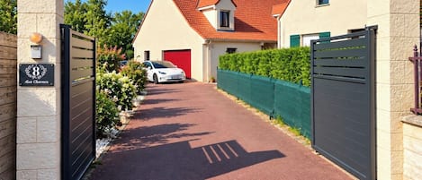 A gated driveway leading to a house with a red roof and a garage.