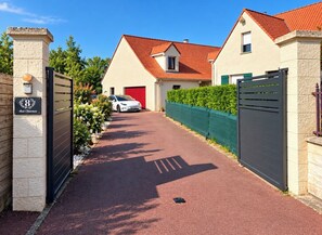 Une allée fermée par un portail mène à une maison avec un toit rouge et un garage.