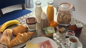 A breakfast table with croissants, cheese, ham, a banana, juice, and a coffee cup. -  Aux Charmes (Isques)