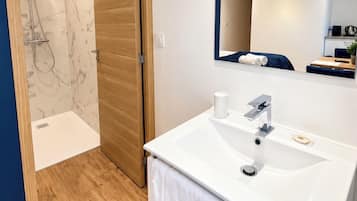 Une salle de bain moderne avec un lavabo blanc, un miroir et un espace douche.