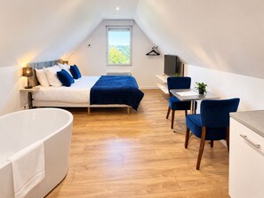 Ett modernt sovrum med en stor säng, en sittgrupp med skrivbord och stolar samt ett separat badrum med badkar.