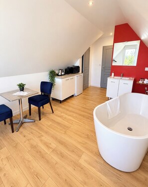 A modern room with a dining area, kitchenette, and a large bathtub. -  Aux Charmes (Isques)