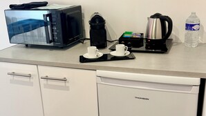 Une petite cuisine équipée d’un four à micro-ondes, d’une machine à café, d’une bouilloire et d’une bouteille d’eau.