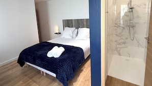 A modern bedroom with a bed, a bedside table, a nightstand, and a built-in shower. -  Aux Charmes (Isques)