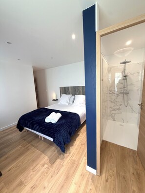 A modern bedroom with a bed, a bedside table, a nightstand, and a built-in shower. -  Aux Charmes (Isques)