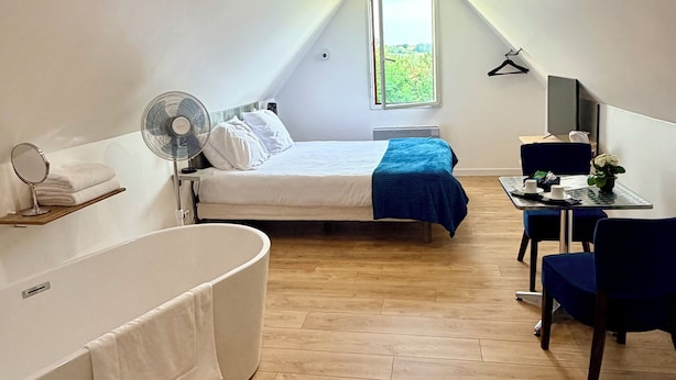 Une chambre moderne et bien éclairée, équipée d’un lit, d’un bureau et d’une chaise, et dotée d’une grande fenêtre et d’un ventilateur.
