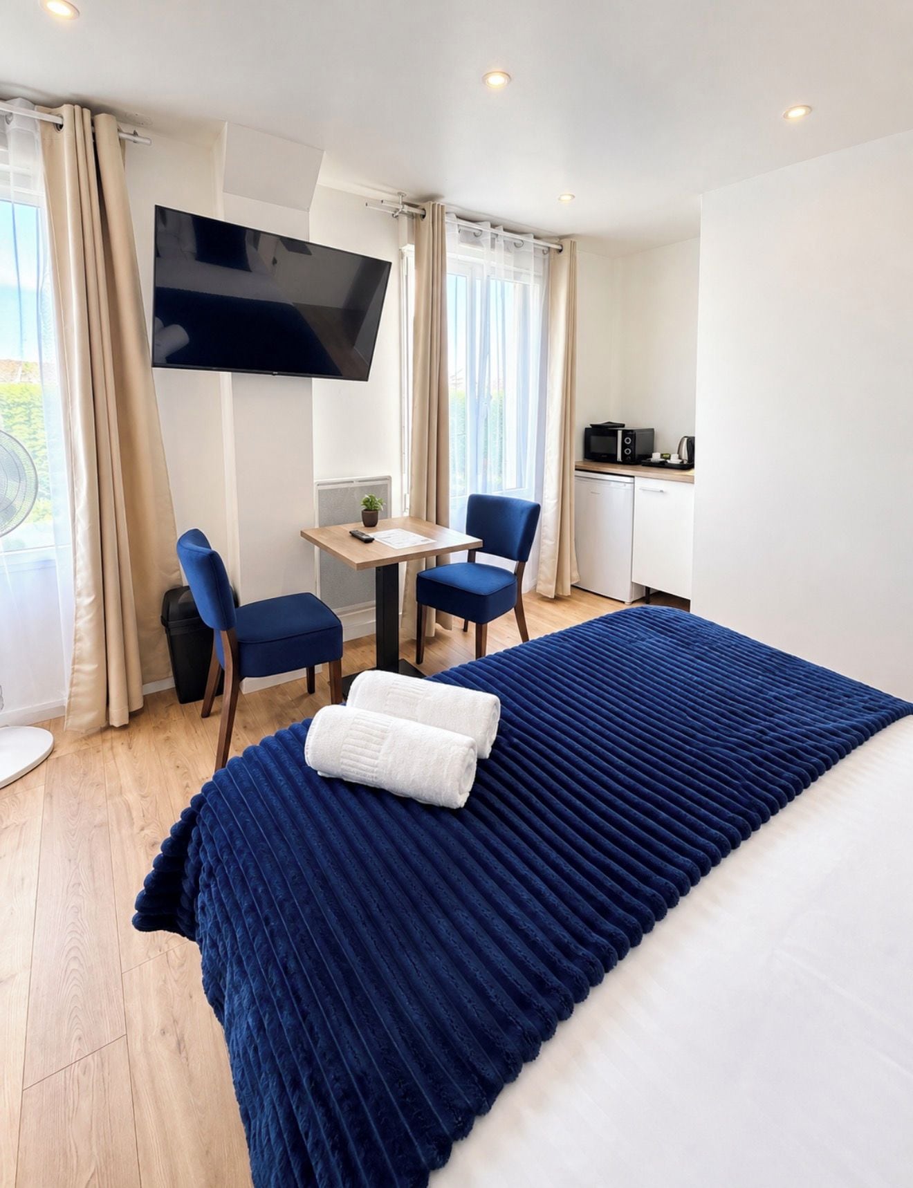 Une chambre d’hôtel comprenant un lit, un bureau, deux chaises, une télévision et une kitchenette.