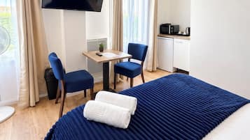 Habitació d'hotel amb un llit, una taula de treball, dues cadires, un televisor i una cuineta.
