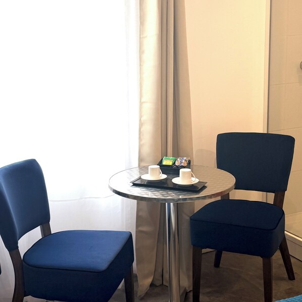 A small round table with two chairs, a tray with cups and a snack pack, and a window with curtains. -  Aux Charmes (Isques)