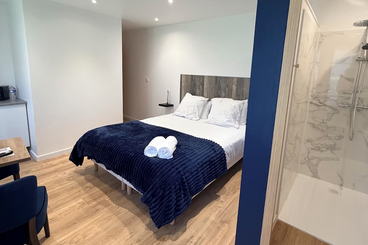 A modern bedroom with a bed, a desk, and a shower area.