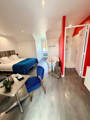 A modern hotel room with a bed, a desk with a chair, a statue, and a shower area. -  Aux Charmes (Isques)