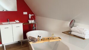 A modern bathroom with a freestanding bathtub, a vanity with a mirror, and a towel rack. -  Aux Charmes (Isques)