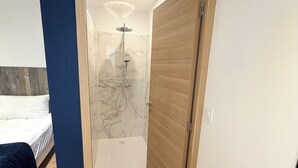 Une chambre avec un lit, une porte en bois, une douche avec un pare-douche en verre et un mur en marbre.