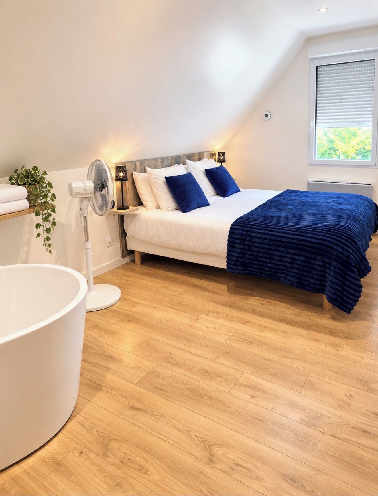 A bedroom with a bed, bedside table, lamp, and a large white bathtub.