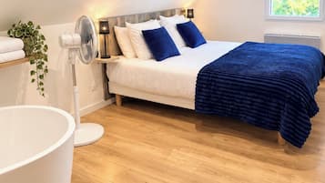 A bedroom with a bed, bedside table, lamp, and a large white bathtub.