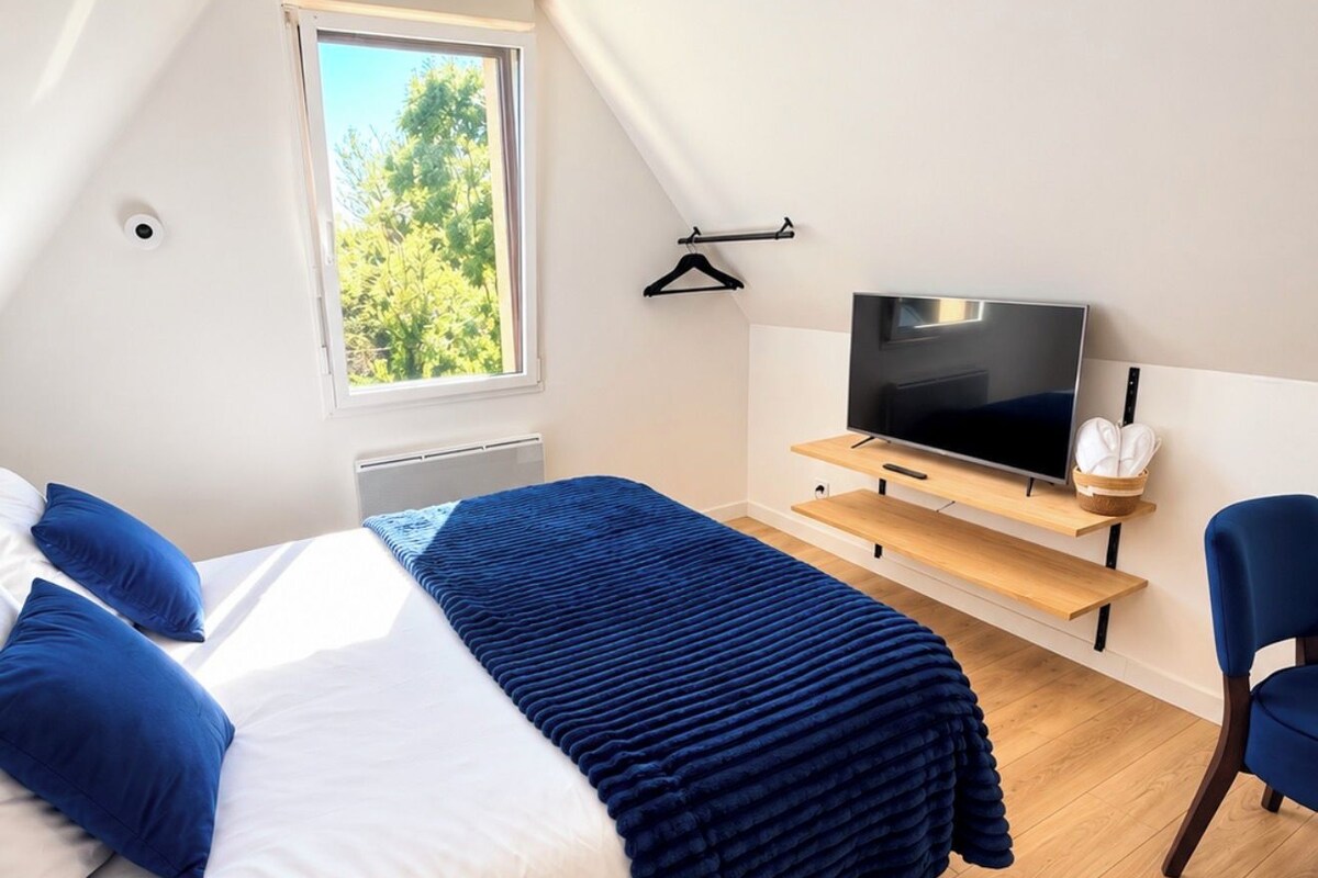 A bedroom with a bed, a TV, a chair, and a window with a view of trees.