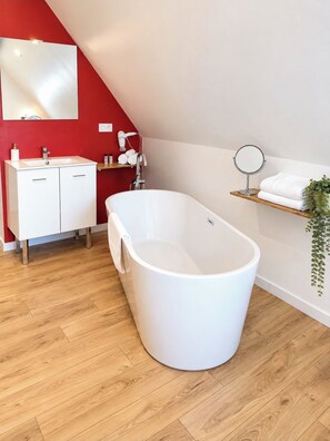 A modern bathroom with a freestanding bathtub, a white vanity with a mirror, and a red accent wall. -  Aux Charmes (Isques)