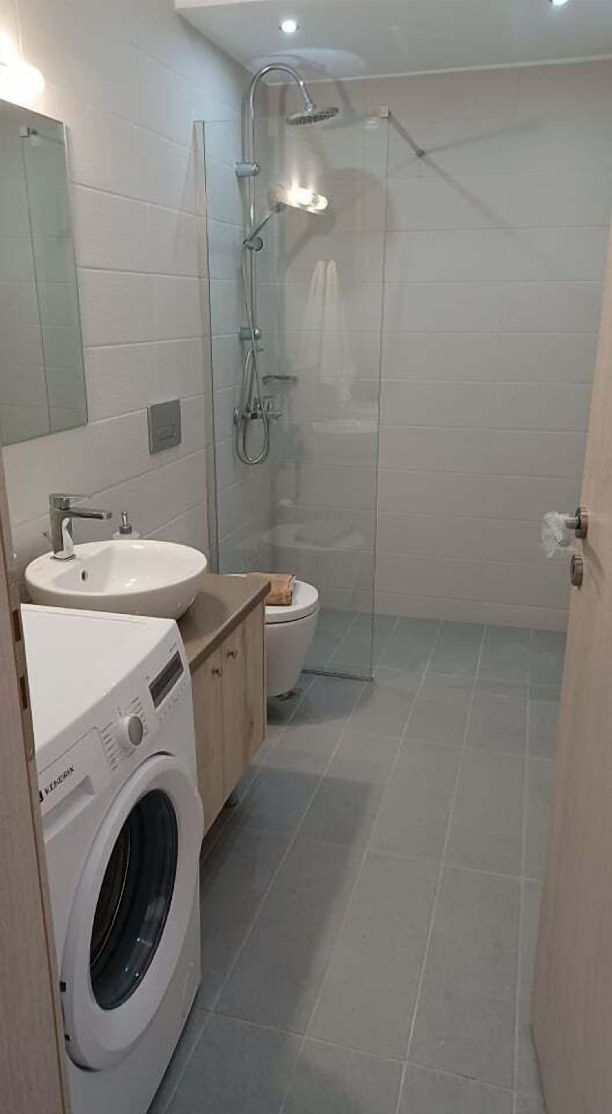 Een moderne badkamer met een ingebouwde wasmachine, een wastafel, een toilet en een douchecabine met glazen wanden.
