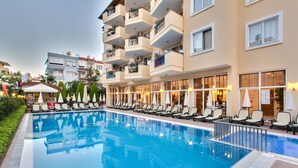 A hotel with a swimming pool, lounge chairs, and a building with balconies. - Novella Apart Hotel (Alanya)