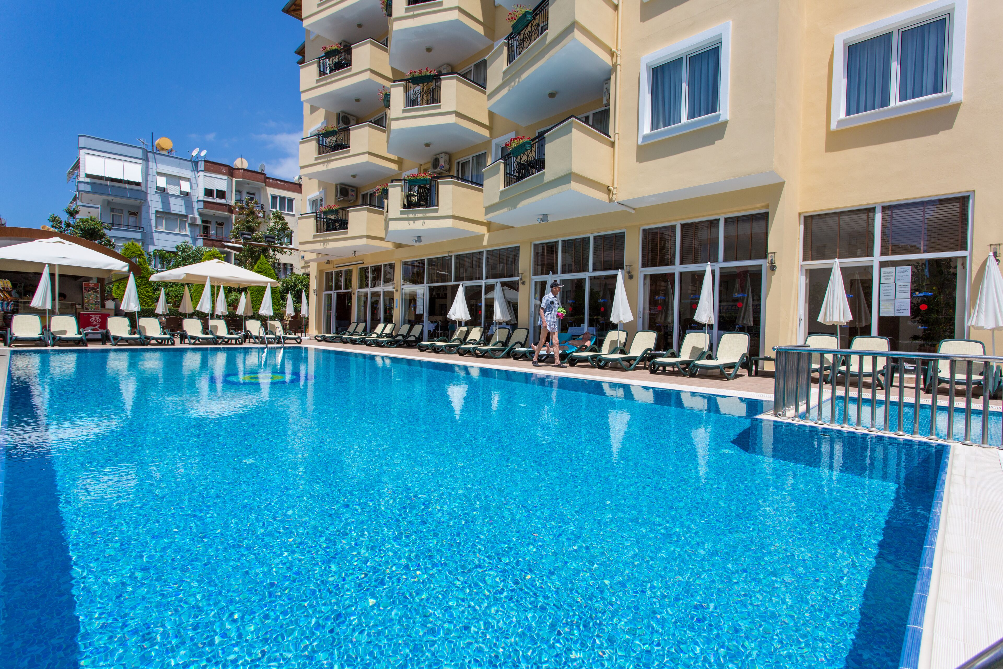 A swimming pool with lounge chairs and umbrellas, surrounded by multi-story buildings with balconies.