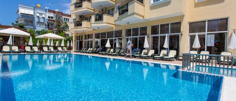 A swimming pool with lounge chairs and umbrellas, surrounded by multi-story buildings with balconies.
