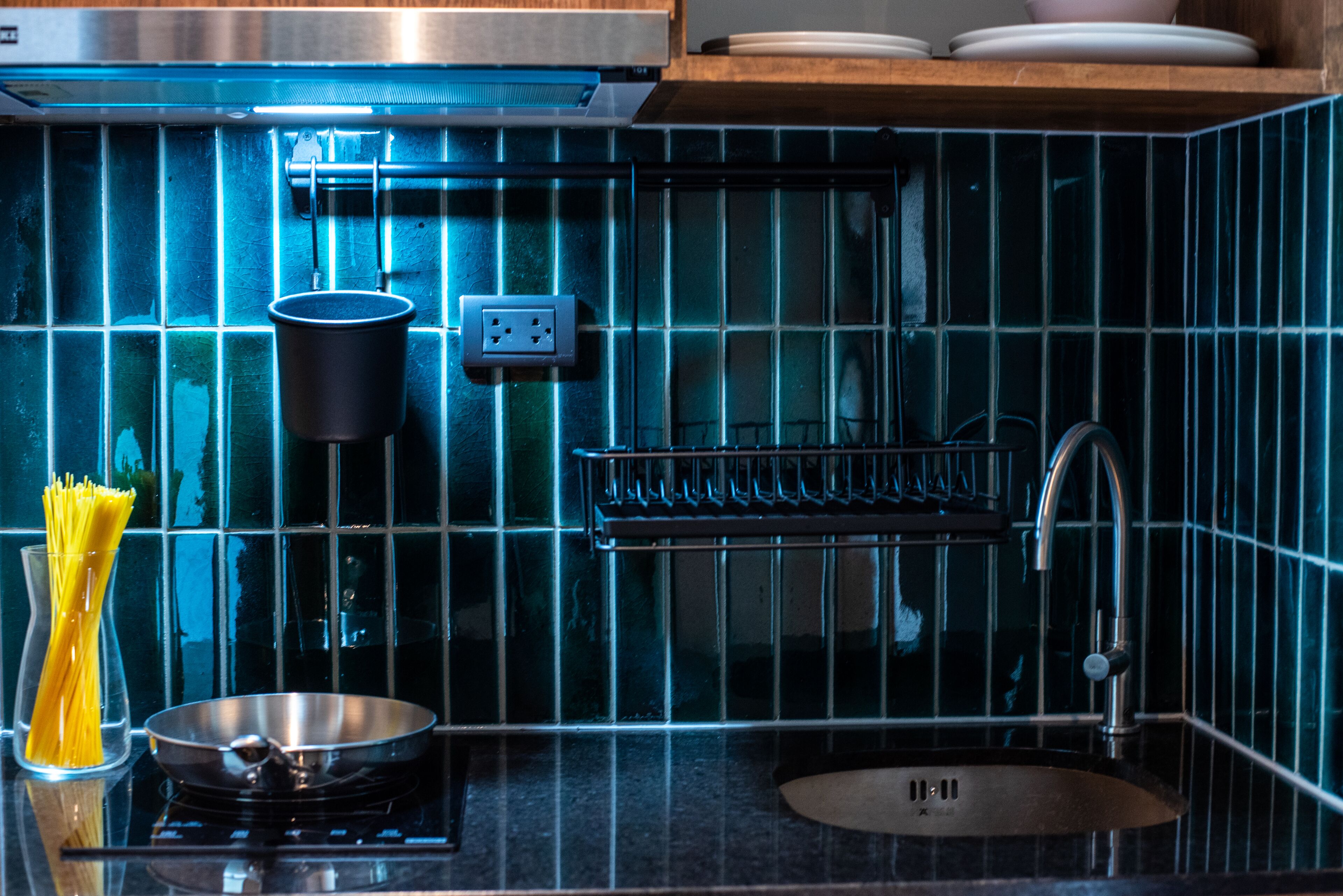Una cocina con salpicadero de azulejos negros, electrodomésticos de acero inoxidable, un colgador para ollas y un tazón de espagueti.