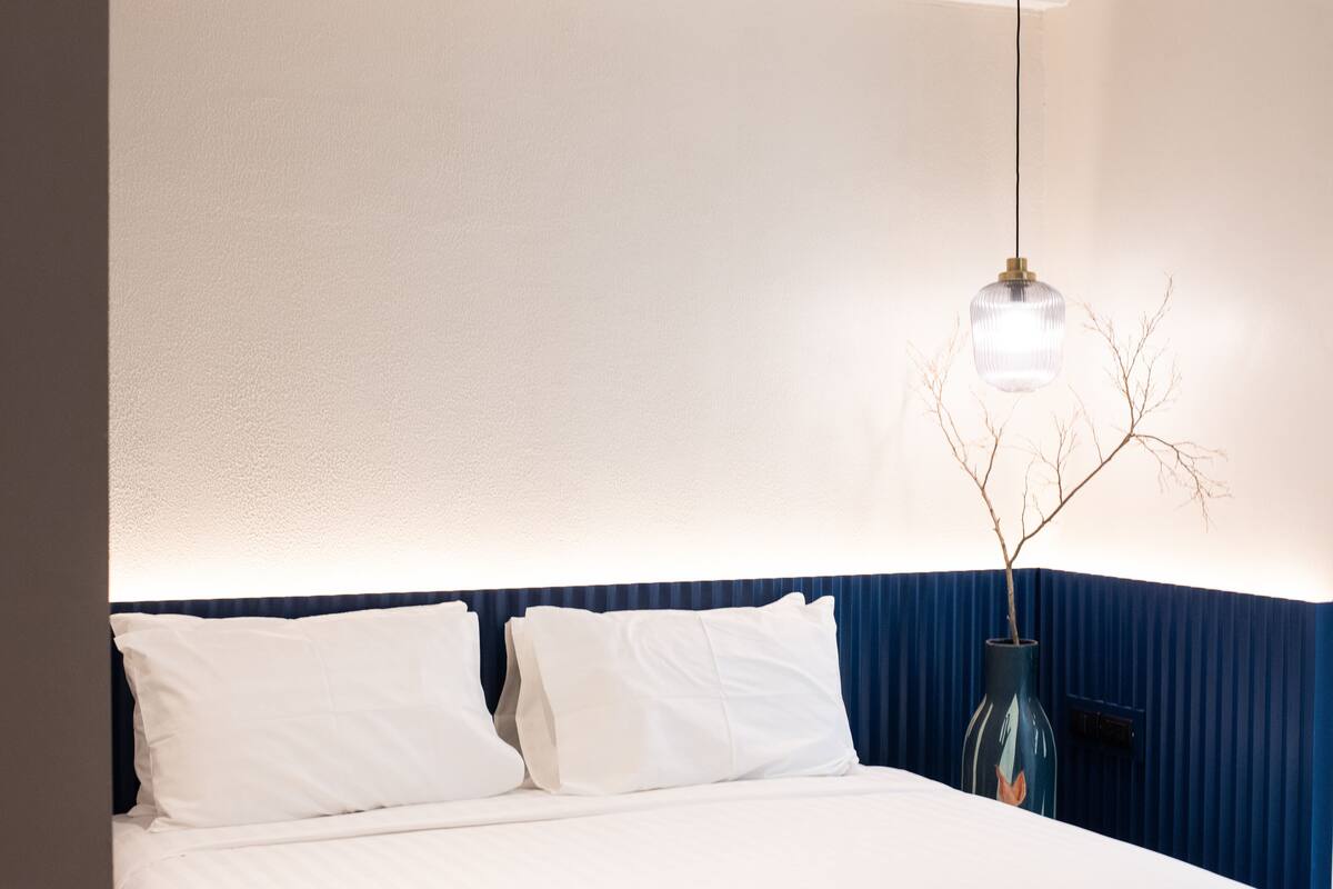 A bed with white linens, a blue accent wall, and a hanging light fixture.