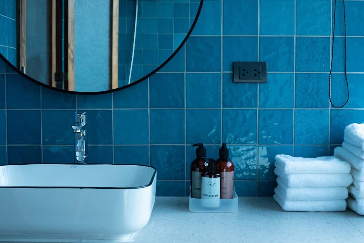 A bathroom with a white sink, blue tiles, a mirror, and a towel rack with white towels.