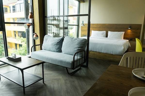Una camera d'albergo moderna con un divano grigio, un letto di legno, un tavolino e una sedia.