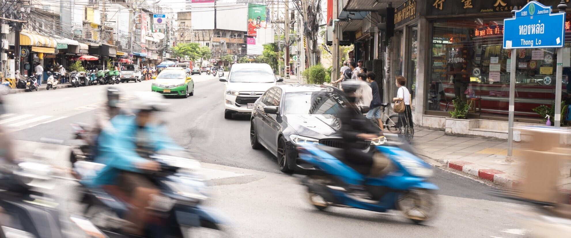 A busy street with motorcycles and cars, shops, and a sign indicating 'Thong Lo'.