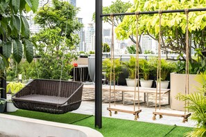 A rooftop garden with a hanging wicker chair, wooden swings, and potted plants. - Karaarom Hotel (Bangkok)